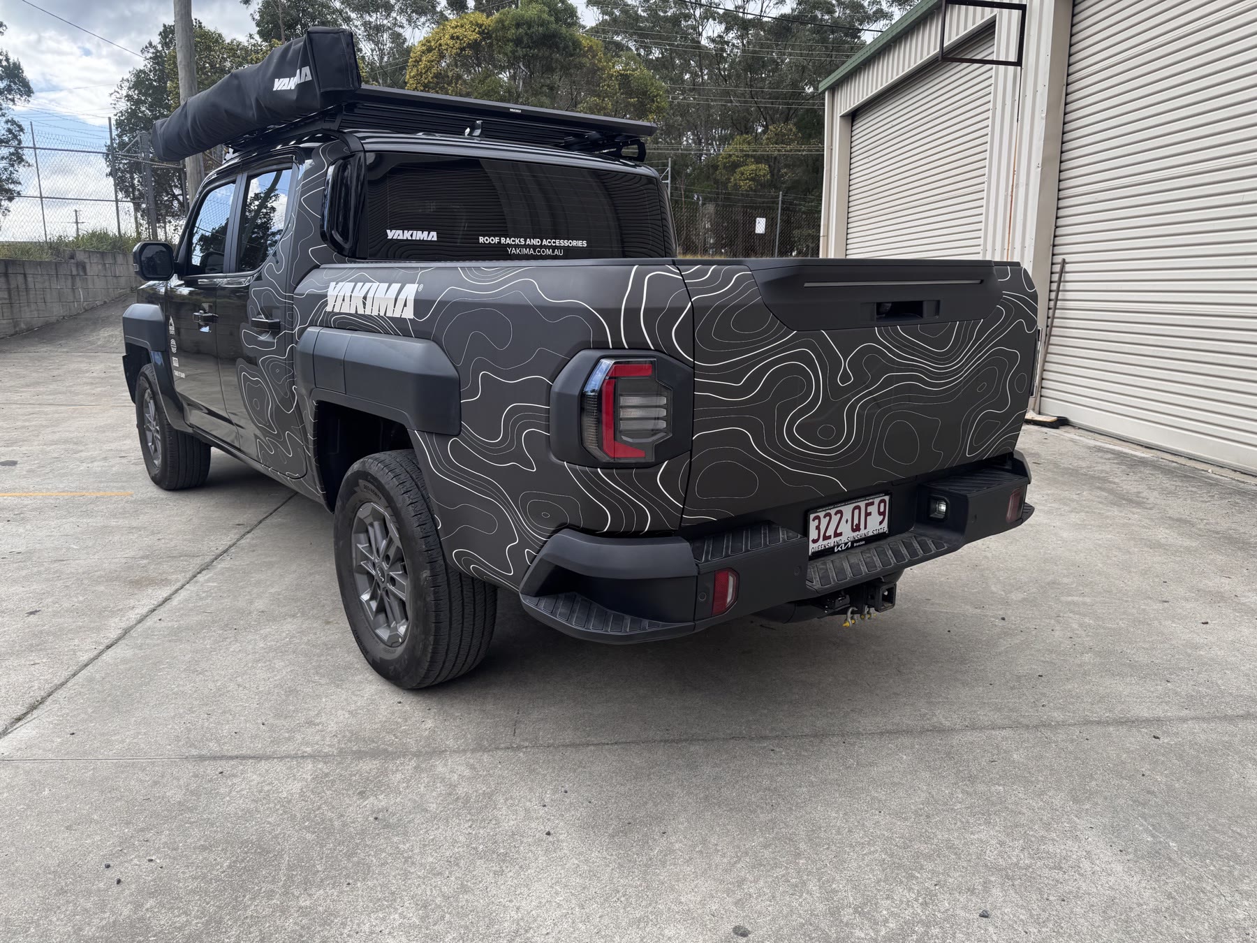 Rear three-quarter view of a dark grey ute with white contour-line graphics and Yakima branding
